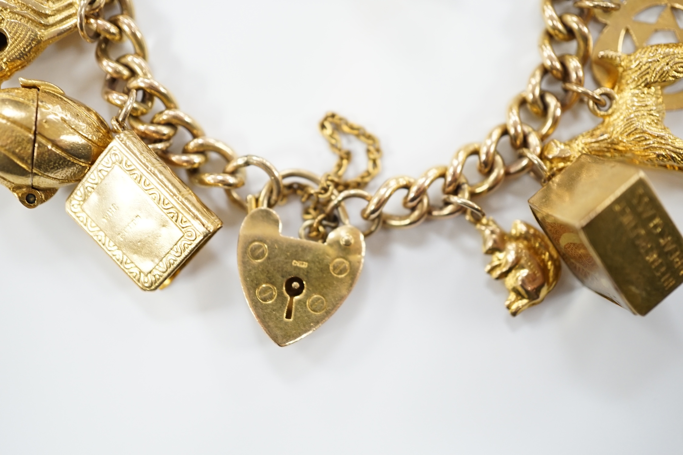 A 9ct gold curb link charm bracelet, with heart shaped padlock clasp and hung with assorted mainly 9ct gold charms